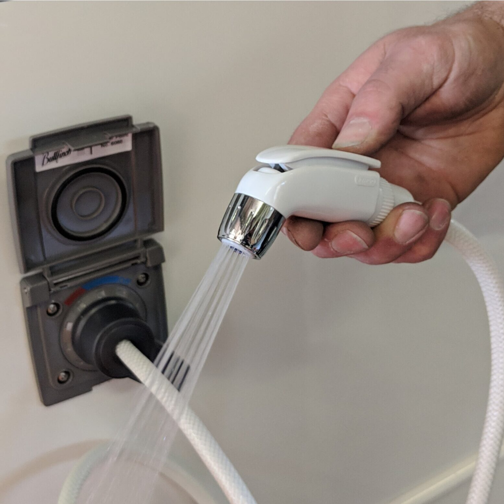 Hand holding a shower head with water flowing, attached to a wall-mounted shower control panel.