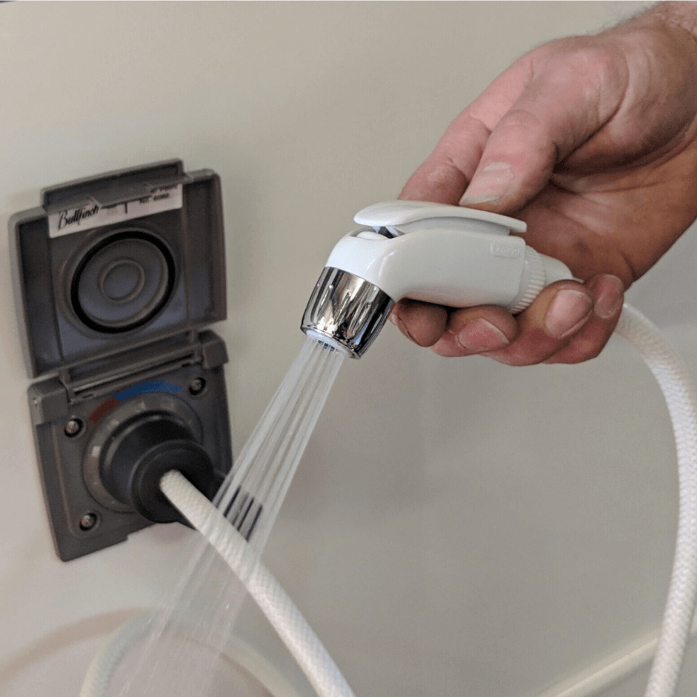 Hand holding a shower head with water flowing, attached to a wall-mounted shower control panel.