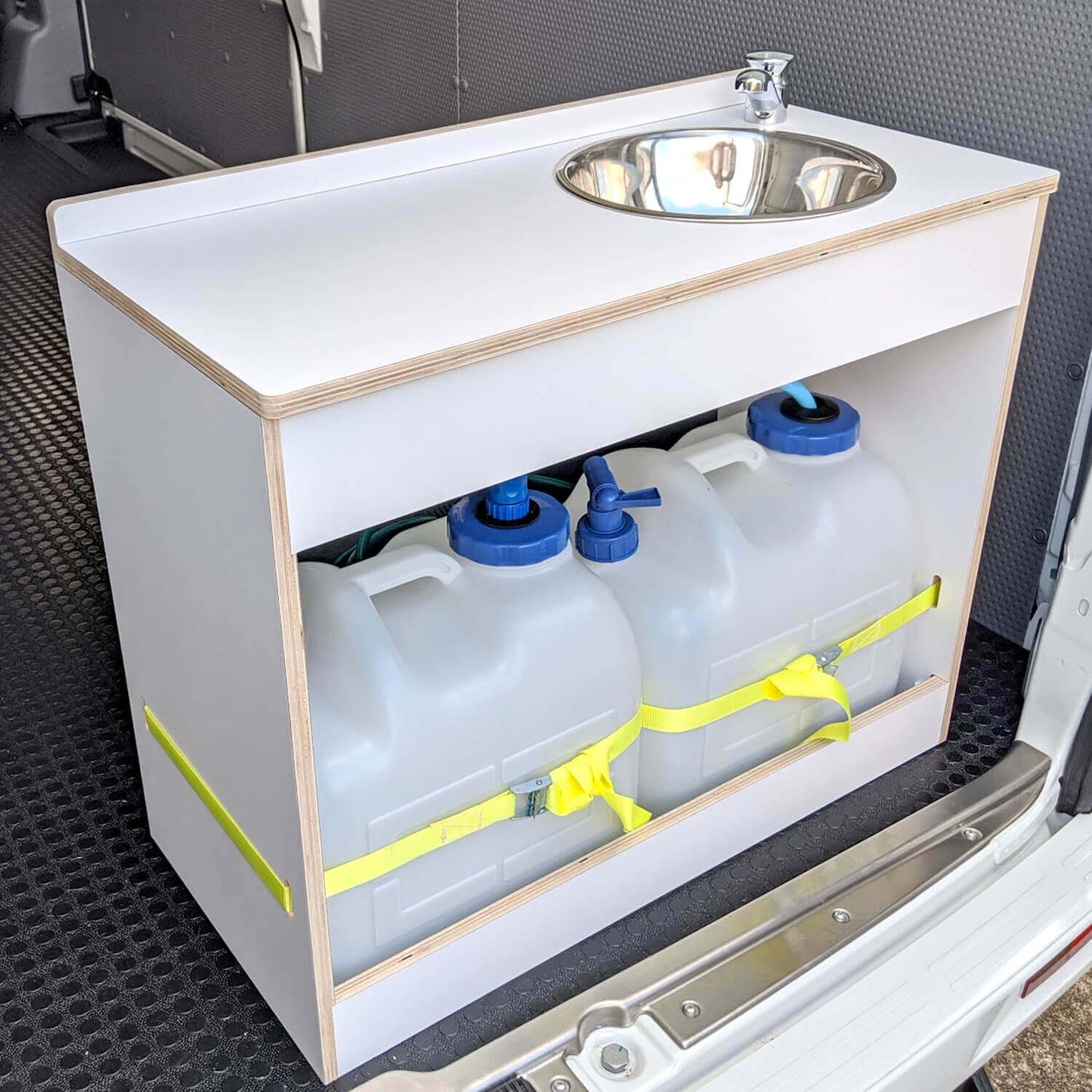 A white plastic sink installed on a wooden cabinet with water tanks below, secured with yellow straps