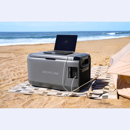 EcoFlow Glacier Portable Fridge Freezer on beach sand with laptop on top, charging via 12V off-grid power