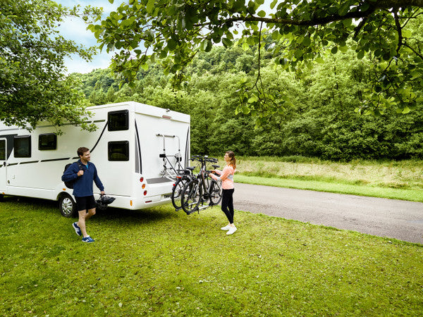 Two people with a white RV and bicycles in a park setting