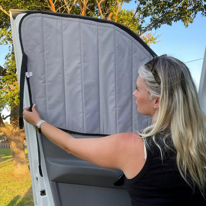 Woman adjusting a gray car sunshade on a vehicle outdoors.
