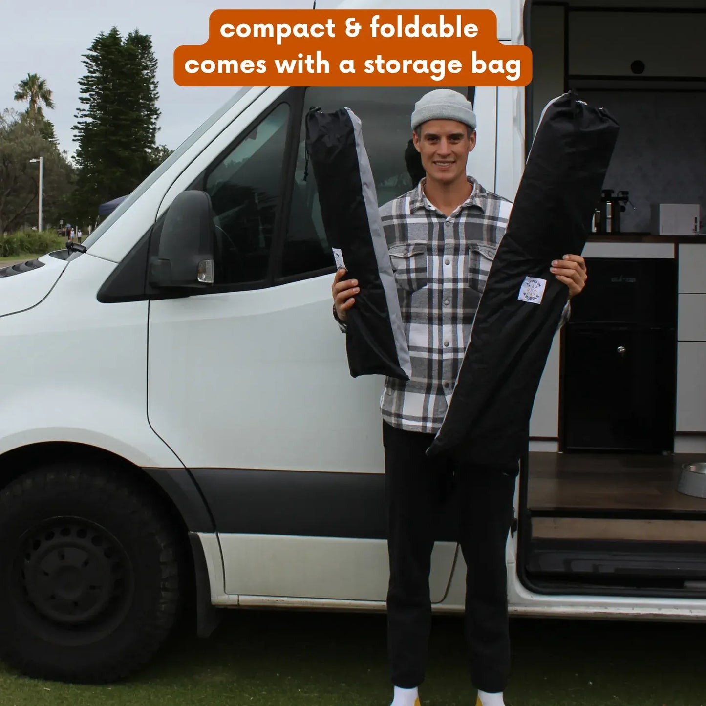 Person holding a large black mat with text about compactness and storage bag, in front of a van.