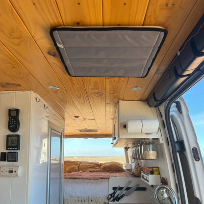 Interior of a van with wooden ceiling, kitchen setup, and view of the desert outside.