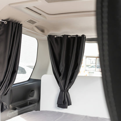 Black blackout curtains installed inside a campervan for privacy and light control around rear windows and sleeping area